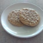 Two soft and chewy old fashioned oatmeal cookies on a white plate.