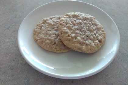 Two soft and chewy old fashioned oatmeal cookies on a white plate.