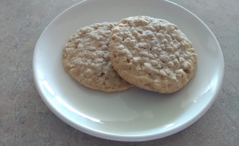 Two soft and chewy old fashioned oatmeal cookies on a white plate.