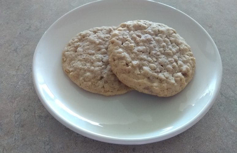 Two soft and chewy old fashioned oatmeal cookies on a white plate.