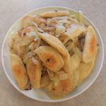 homemade pierogis with sauteed onion on a white plate.