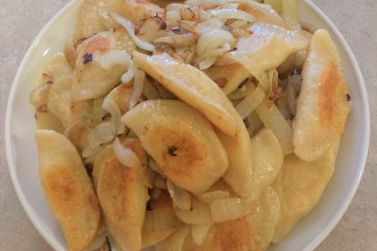 homemade pierogis with sauteed onion on a white plate.