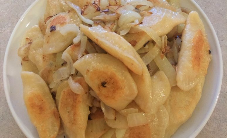 homemade pierogis with sauteed onion on a white plate.