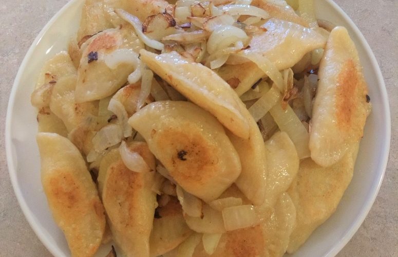 homemade pierogis with sauteed onion on a white plate.