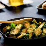 Cast iron pan with fried brussel sprouts and a wooden spoon resting in it.