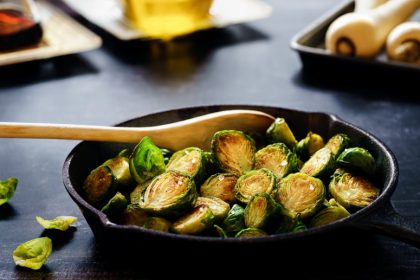 Cast iron pan with fried brussel sprouts and a wooden spoon resting in it.