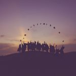 Graduates throwing their caps in the air at sunset.