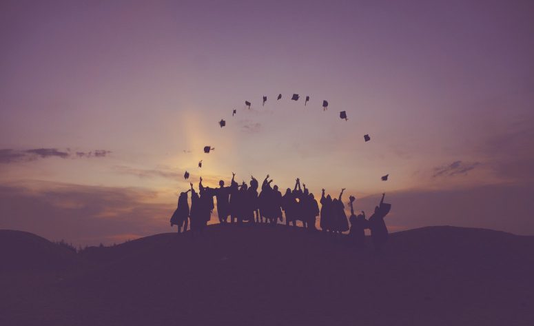 Graduates throwing their caps in the air at sunset.