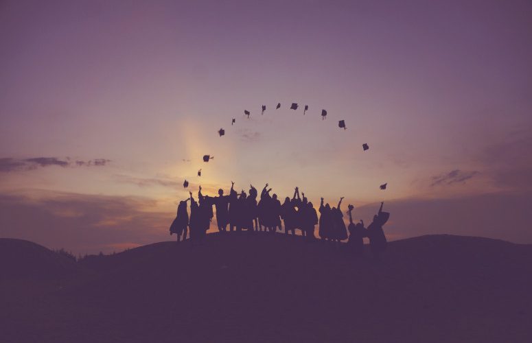 Graduates throwing their caps in the air at sunset.